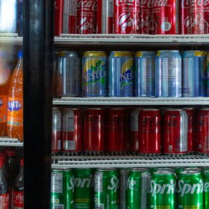 A variety of soda cans, including Coke, Sprite, and Fanta, in a refrigerated display.
